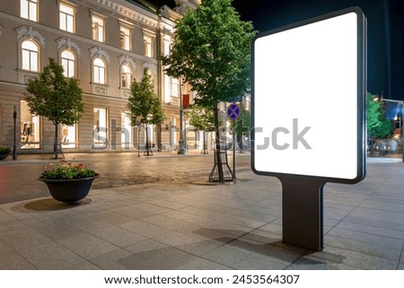Blank Vertical Outdoor Poster Mockup On Old Town Street At Night. Advertising Lightbox In The Background Of A Luxury Mall