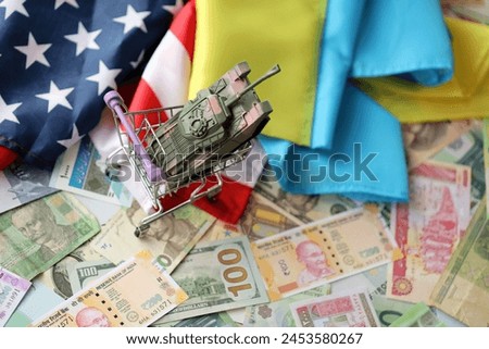 Toy tank on US flag and ukrainian flag on many banknotes of different currency. Background of war funding and military support between United States and Ukraine