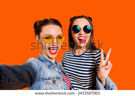 Glad positive grinning adorable good-looking funky funny two lady isolated on yellow vivid background in casual denim jeans wear trendy glasses spectacles take picture on cellular give v-sign