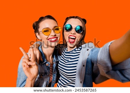 Two glad positive grinning lady stand in glasses spectacles street style stylish trendy cool casual denim jeans clothes isolated on yellow background in take picture on cellular make hollywood smile