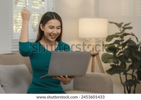 a beautiful Asian teenage girl is having fun watching entertainment in  an application on laptop at home on the sofa, a beautiful female spend a weekend on the couch in ultimate bliss in an apartment.