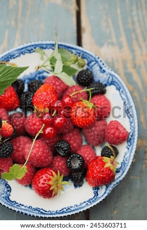 Ripe raspberries, strawberry and wild blackberries on a vintage plate