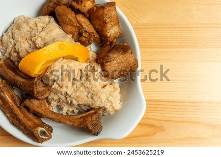 A plate of fried pork with Alentejo-style migas, a dish made from breadcrumbs, garlic, and herbs, topped with an orange slice. Captured in a rustic restaurant setting, it exudes warmth and tradition.
