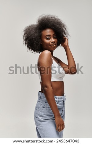 A young African American woman with a curly afro hair posing for a photograph in a studio setting.