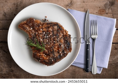 Top view of Flavored Whole rib eye beef on white round plate with cutlery and napkin on wooden background