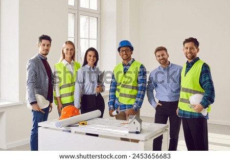 Team of construction workers and engineers in hardhats discussing project. Group of cheerful professional builders in hardhats looking at camera at construction site