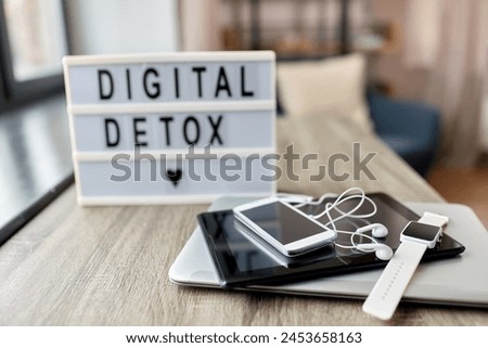 technology concept - digital detox words on light box and different gadgets on blue background
