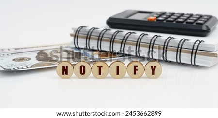 Business and finance concept. On a high surface lie a notepad, a calculator, dollars and wooden circles with the inscription - NOTIFY Royalty-Free Stock Photo #2453662899