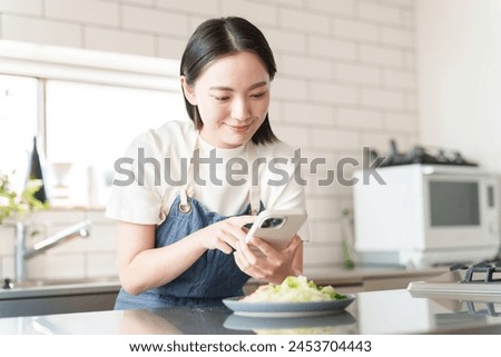young asian woman taking picture of food with smartphone in kitchen