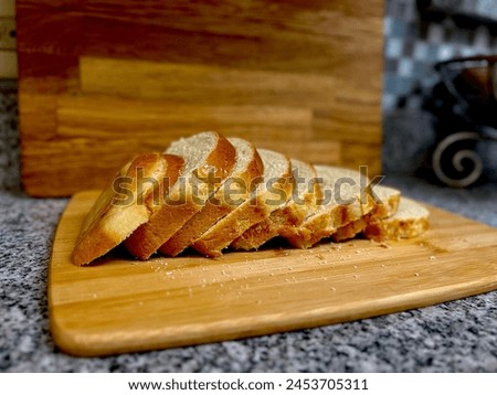 A loaf of freshly homemade sandwich white wheat bread sliced on a wooden cutting board over the granite kitchen counter.  Aesthetic food photography. Writing and copy space.