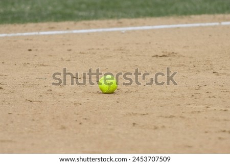 abstract close up of a yellow softball on the infield dirt of a field 