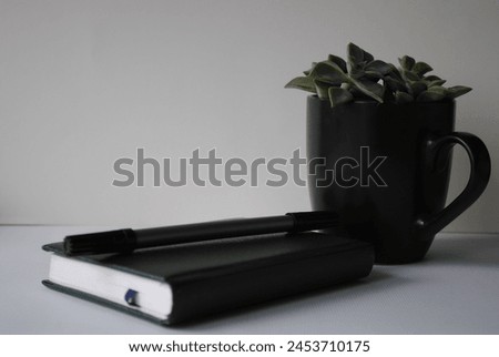Notepad, pen and black cup with green leaves on a white background. Place for text, background. Royalty-Free Stock Photo #2453710175