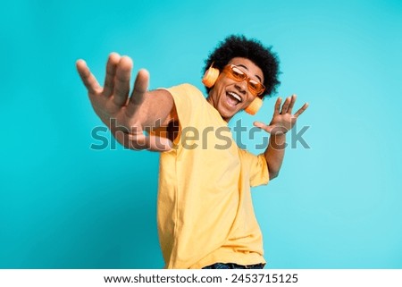Portrait of overjoyed man with afro hairstyle wear oversize t-shirt in glasses enjoy music in headphones isolated on teal color background
