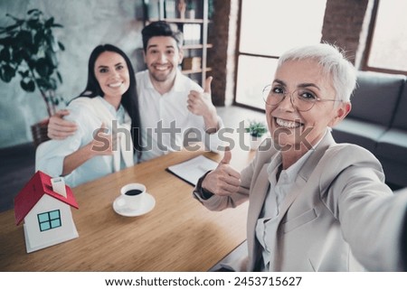 Portrait of young couple meeting realtor lady take selfie show thumb up desk loft interior office indoors