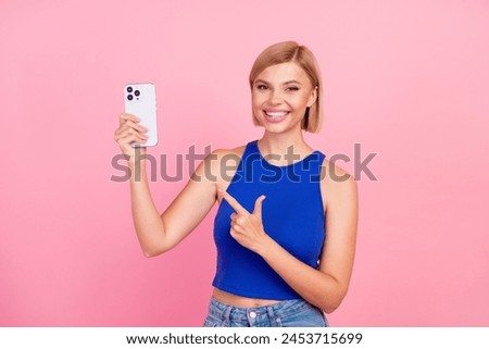 Photo of pretty young woman indicate finger smart phone wear blue top isolated on pink color background