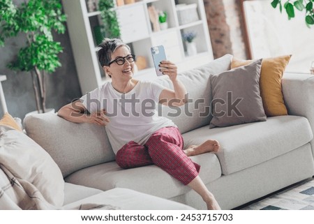 Full size photo of nice senior woman video call sit sofa dressed white clothes cozy living room home house flat indoors pension concept