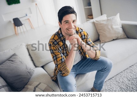 Photo of handsome cheerful guy dressed plaid shirt smiling arms chin relaxing sofa enjoying weekend indoors room home house Royalty-Free Stock Photo #2453715713