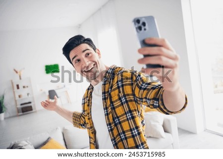 Photo of handsome cheerful guy dressed plaid shirt showing new apartment recording video modern gadget indoors room home house