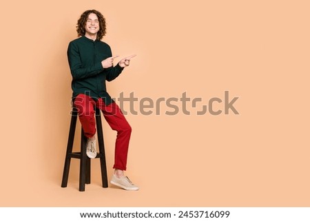 Photo portrait of handsome young guy sit chair point empty space dressed stylish green garment isolated on beige color background