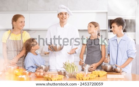 Pleasant and sociable young man, professional chef, leading culinary courses, imparting cooking skills to group of interested tweens.. Royalty-Free Stock Photo #2453720059