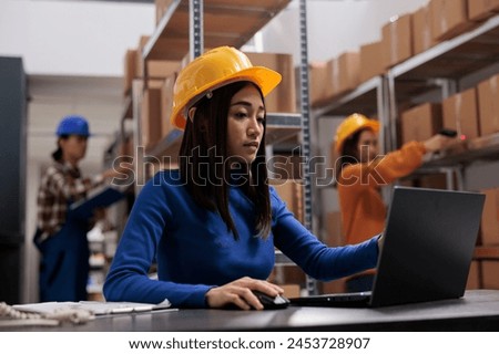 Asian retail storehouse employee analyzing orders checklist on laptop while working in storage room. Warehouse manager supervising inventory management while using computer Royalty-Free Stock Photo #2453728907