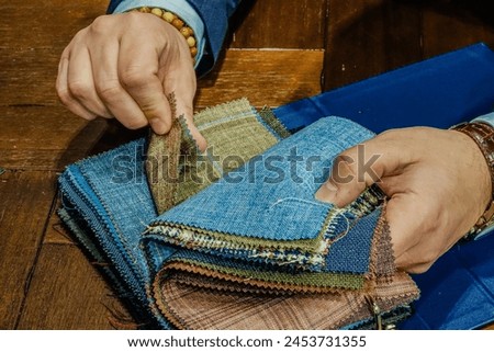 A detailed view of a craftsperson's hands as they meticulously sort through a stack of colorful fabric samples, illustrating creativity and skill in textile design. Royalty-Free Stock Photo #2453731355