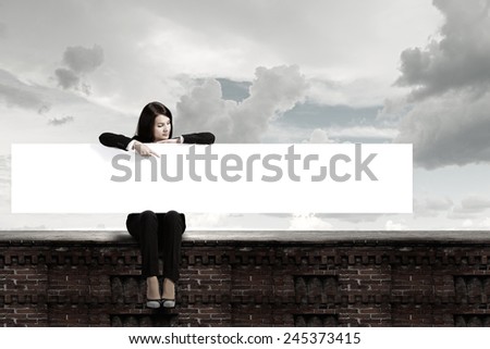 Young woman sitting on top of building with blank banner