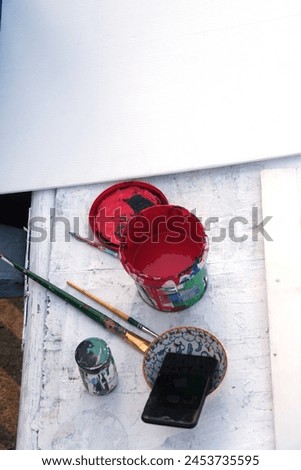 A messy can of red paint, a paintbrush, and a white plastic sheet for writing on signs.