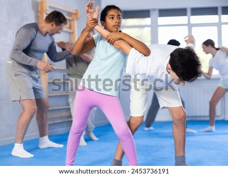 Determined black tween girl practicing armlock, painful control move to hold and immobilize opponent, in training bout with boy during self defence course in gym .. Royalty-Free Stock Photo #2453736191
