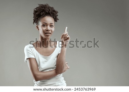 Thoughtful young Black woman gestures an idea, poised in a white tee Royalty-Free Stock Photo #2453763969