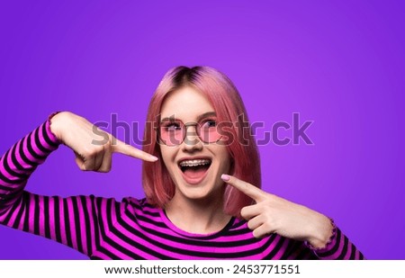 Dental dent care ad concept image - look up pink funny beautiful woman in metal braces wear sunglasses, pointing white teeth smile. Isolated violet purple background. Positive optimistic.