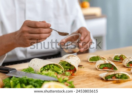 chef make tortilla wrap vegetable salad slice by knife on cutting board and mix sour salad dressing in small bowl glass with wine and olive oil. tortillas wrap vegetable and juicy liquid sour dressing