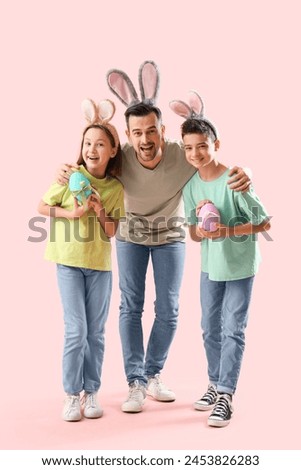 Little children and his father in bunny ears with Easter eggs on pink background