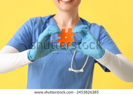 Female doctor with hashtag sign on yellow background, closeup