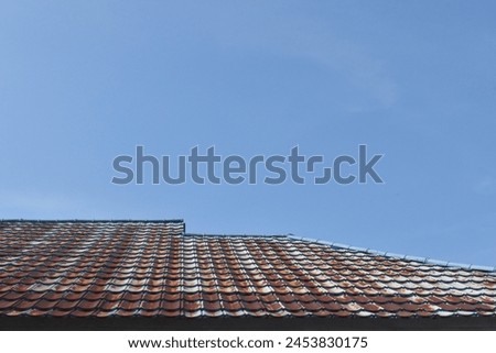 the rusty surface of the roof tiles is brown under the bright blue sky.  the roof of the house is starting to turn brown and worn out.