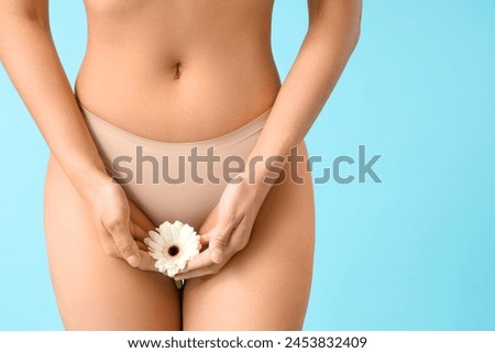 Beautiful young woman in panties with gerbera flower on blue background, closeup Royalty-Free Stock Photo #2453832409