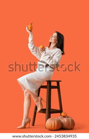 Beautiful young woman with pumpkins sitting on orange background