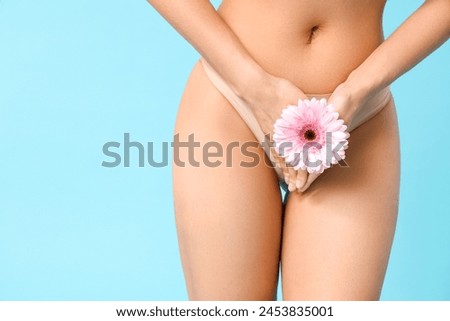 Beautiful young woman in panties with gerbera flower on blue background, closeup Royalty-Free Stock Photo #2453835001