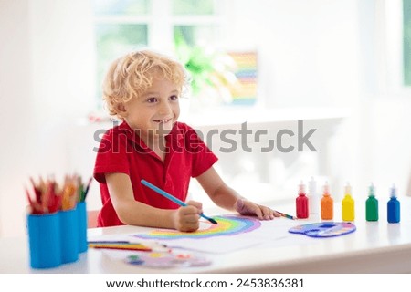 Kids paint. Child painting in white sunny study room. Little boy drawing rainbow. School kid doing art homework. Arts and crafts for kids. Paint on children hands. Creative little artist at work.