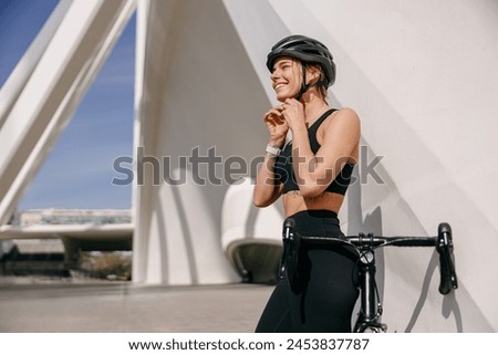 Smiling female cyclist is putting helmet on head before going to go ride by bicycle in city