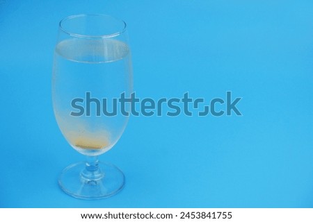 Vitamin C effervescent tablet dissolving in glass of water on blue background.