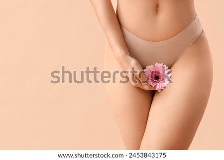 Beautiful young woman in panties with gerbera flower on beige background, closeup Royalty-Free Stock Photo #2453843175