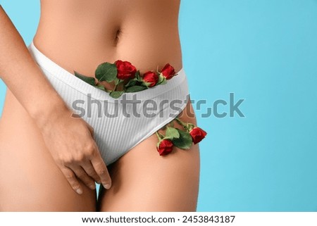 Beautiful young woman in panties with rose flowers on blue background, closeup Royalty-Free Stock Photo #2453843187