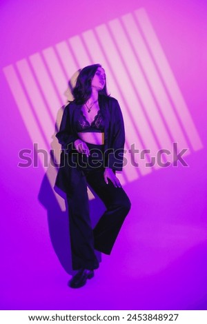 A beautiful young woman in a black suit stands on a white background. Hard light.