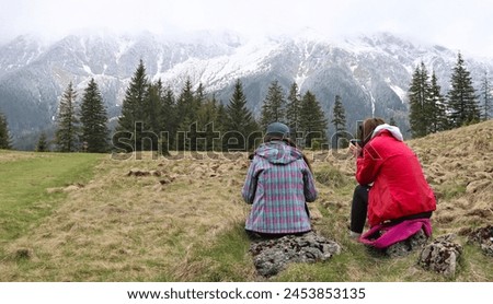 Two girls on a mountain hike. Girls in mountain jackets looking at the mountain landscape and mountains in the fog. Two tourists hiking in a foggy weather in a mountain meadow. Romania Mountains