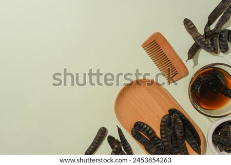 Wooden tray decorated by some black locust fruit with empty space, a glass bowl with locust liquid, a wooden comb, all items placed in bottom corner of the picture. Copy space, top view