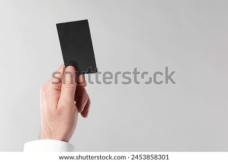 Man holding blank business card on light grey background, closeup. Space for text