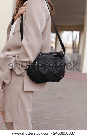 Unrecognizable brunette woman wearing trendy business beige pants suit. Carrying black bag over her shoulder. Posing on beige background outside. Side view. Copy, empty space for text
