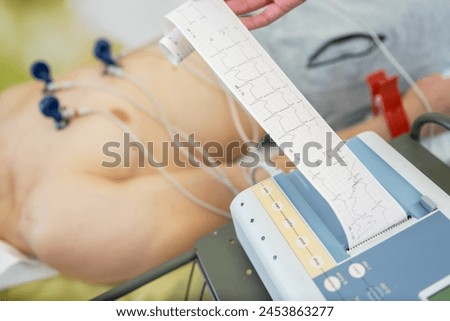 A patient undergoing an electrocardiogram test with electrodes attached to the chest, as a healthcare professional examines the ECG readout. Royalty-Free Stock Photo #2453863277