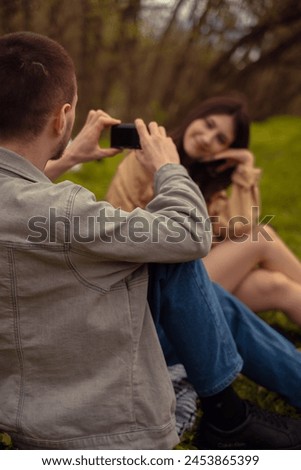 A man takes a photo of his girlfriend on his phone. A young couple camping in the forest, enjoying active outdoor leisure and travel adventures. Valentine's Day
